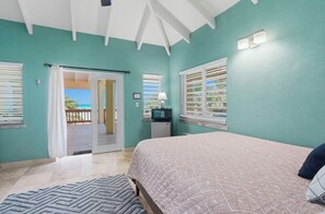 A bedroom with a bed, a television, and a view of the ocean through a sliding door.
