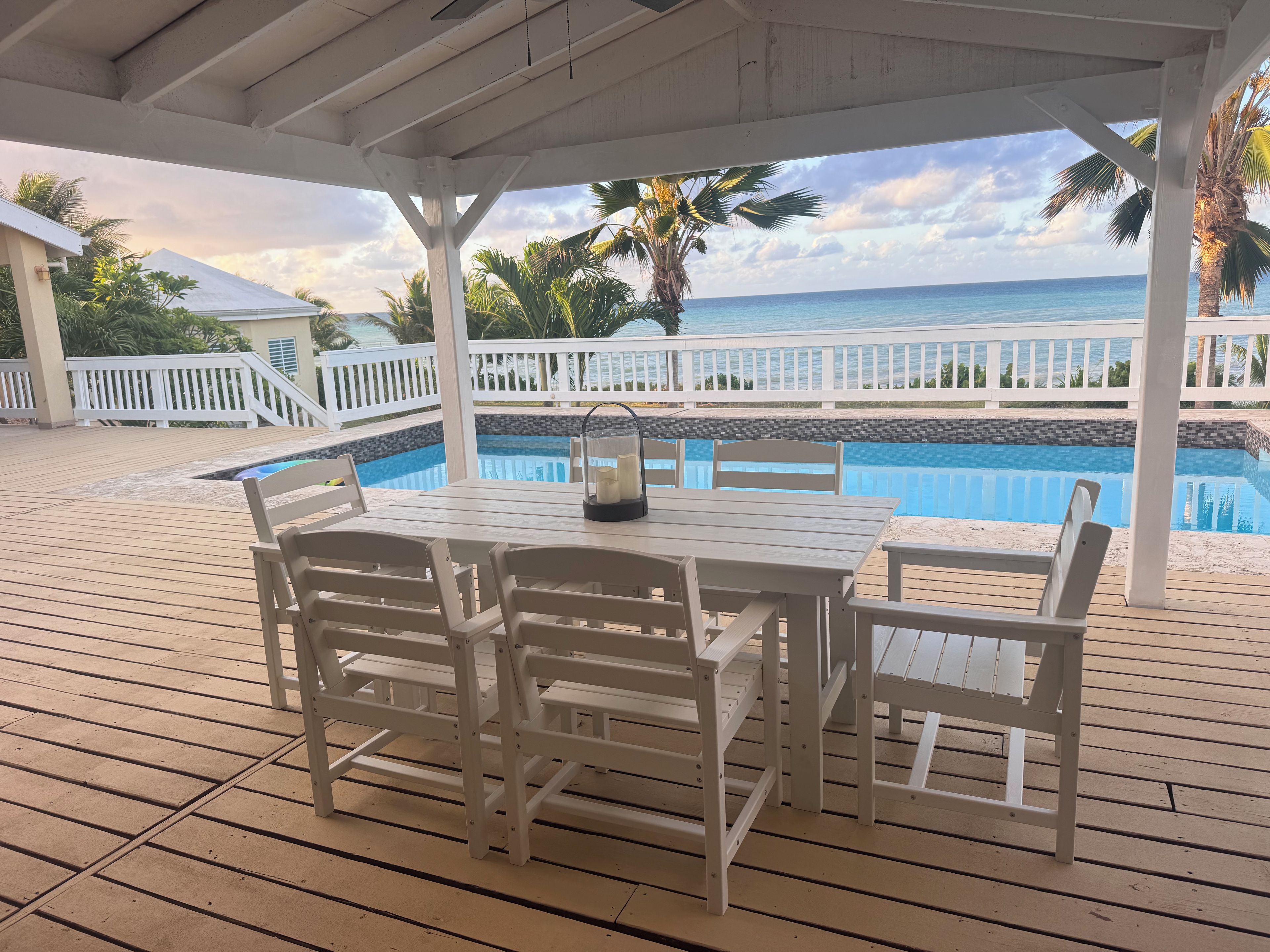 A covered outdoor area with a pool, white furniture, and a view of the ocean.