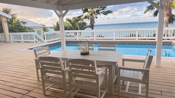 A covered outdoor area with a pool, white furniture, and a view of the ocean.