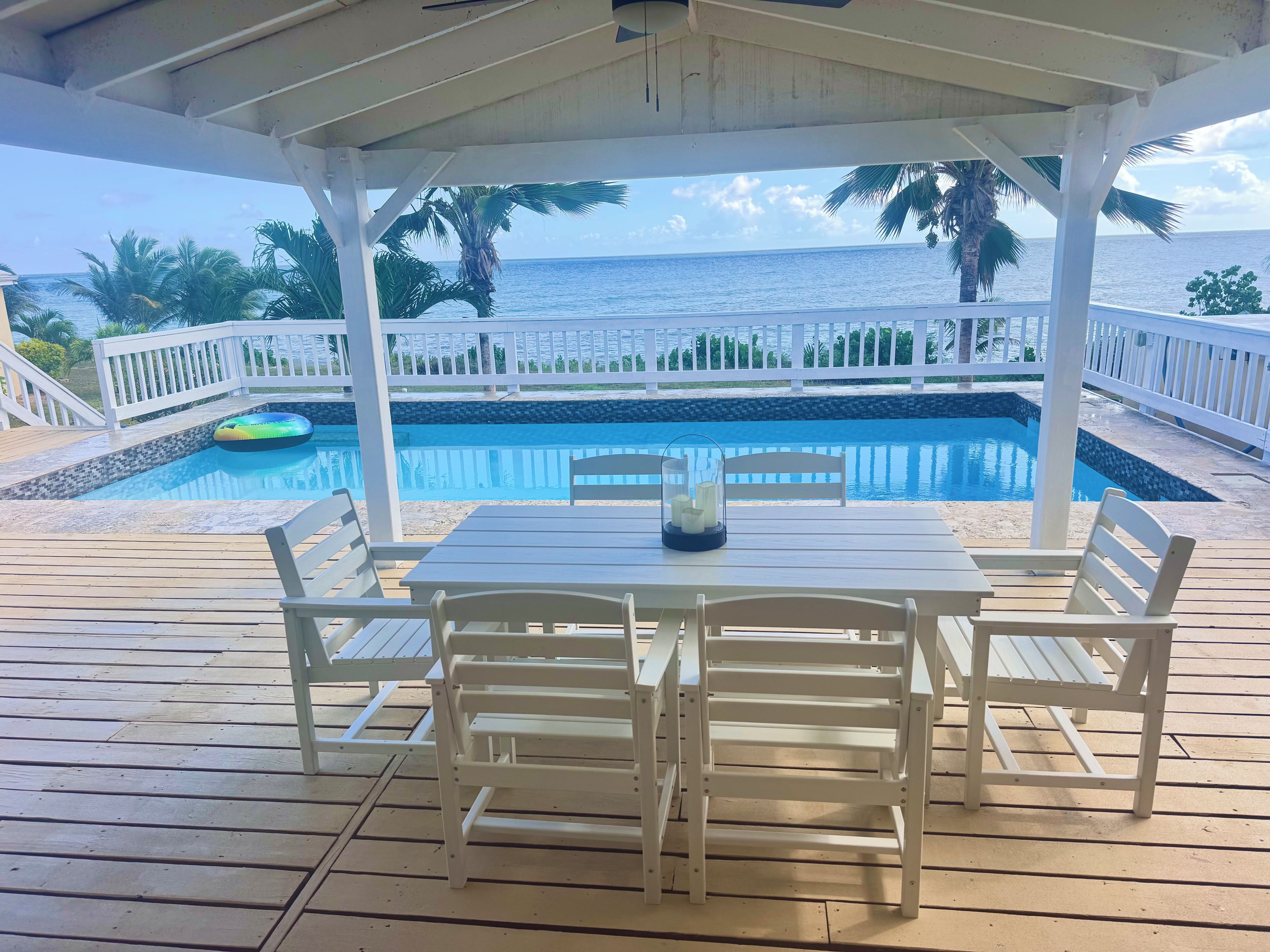 A covered outdoor area with a pool, white furniture, and a view of the ocean.