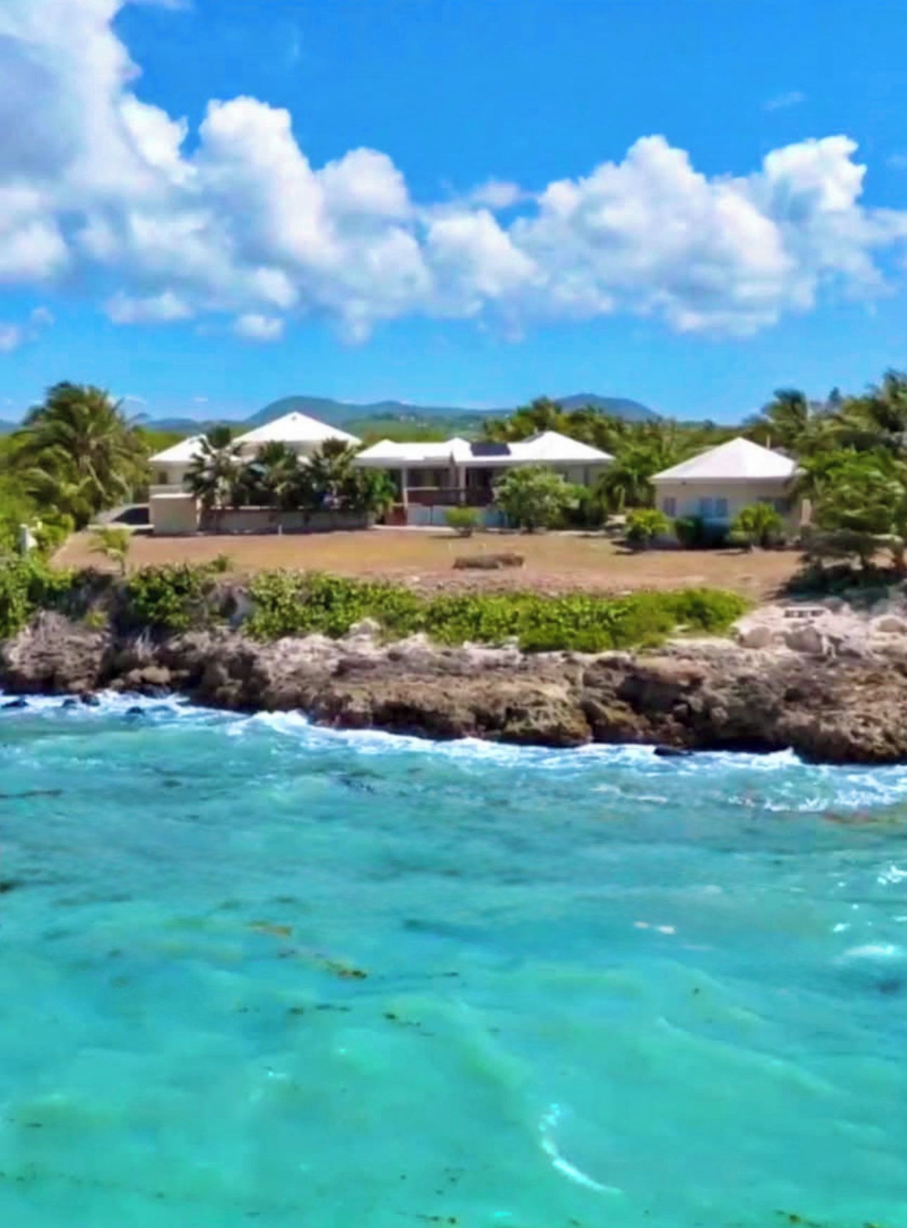 A coastal property with a view of the ocean, a rocky shoreline, and a series of buildings with white roofs.