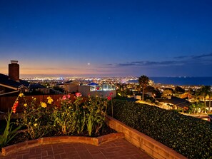 A residential area with a view of a cityscape at dusk, featuring a well-maintained garden with flowering plants and a brick pathway. -  Views!!! Single level La Jolla, CA. home with panoramic ocean and city views! (San Diego)