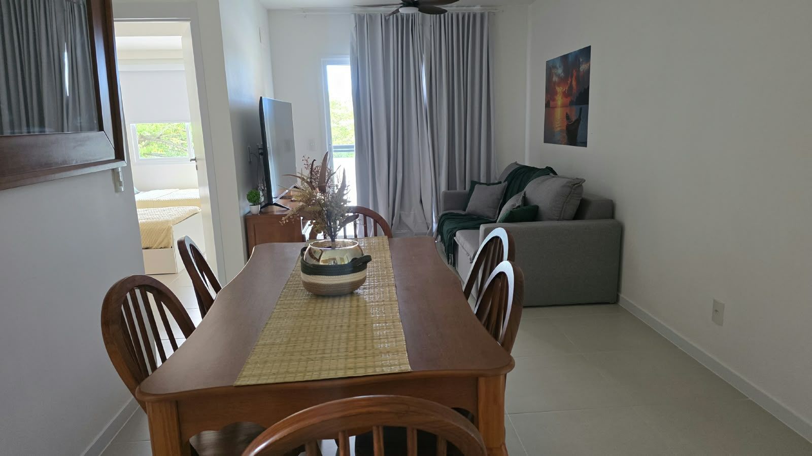 A dining area with a wooden table, chairs, and a decorative bowl. A sofa and curtains are visible in the background.