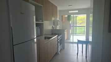 A modern kitchen with a refrigerator, microwave, stove, and sink. There is a dining area with a table and chairs.