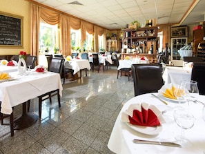 Un restaurante con varias mesas preparadas para comer, una zona de bar con botellas y un menú en una pizarra en la pared.