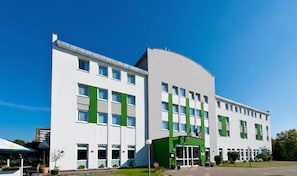 Un edificio moderno con fachada curva, múltiples ventanas y entrada verde.