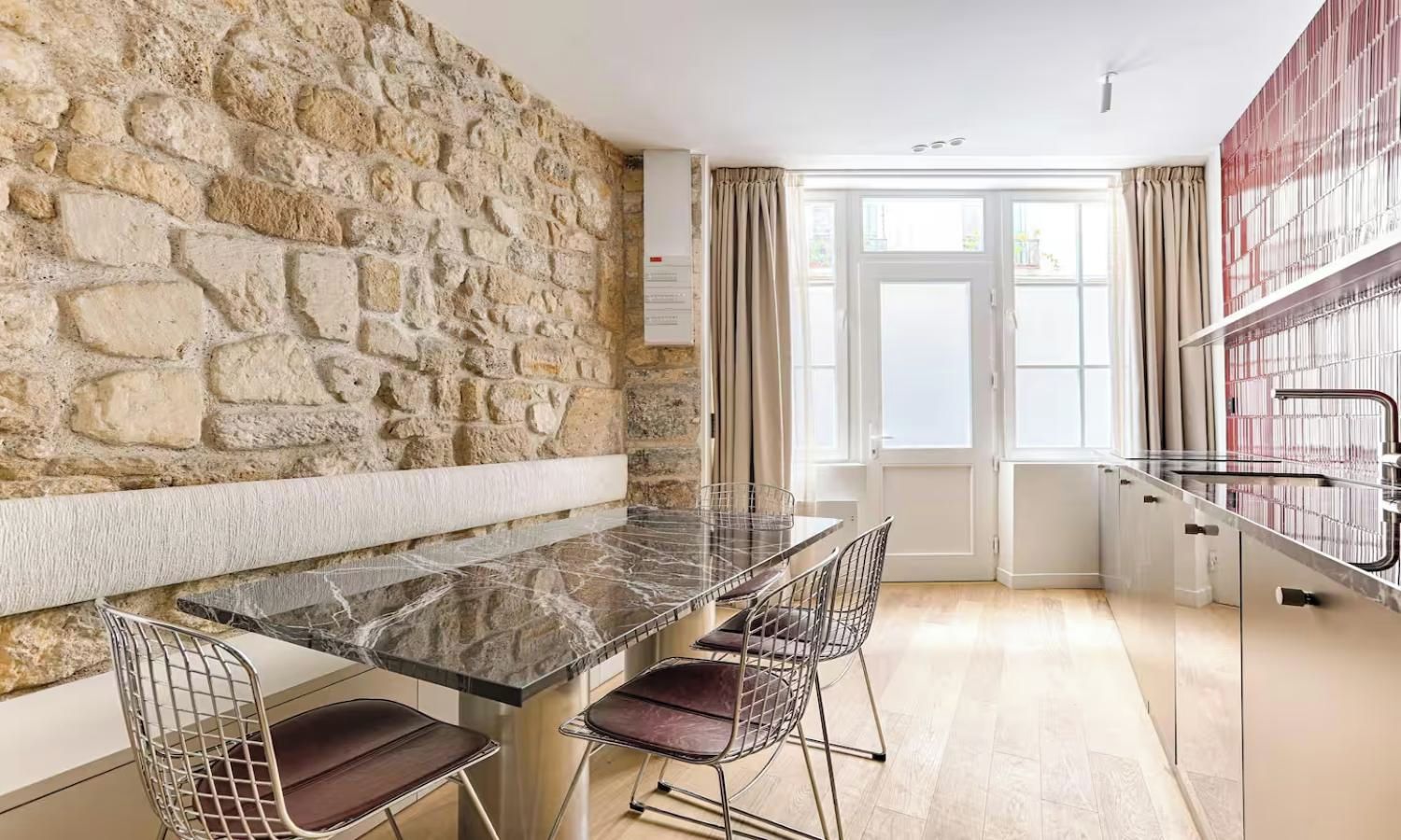 A modern kitchen with a stone wall, a marble countertop, and a dining area with metal chairs.