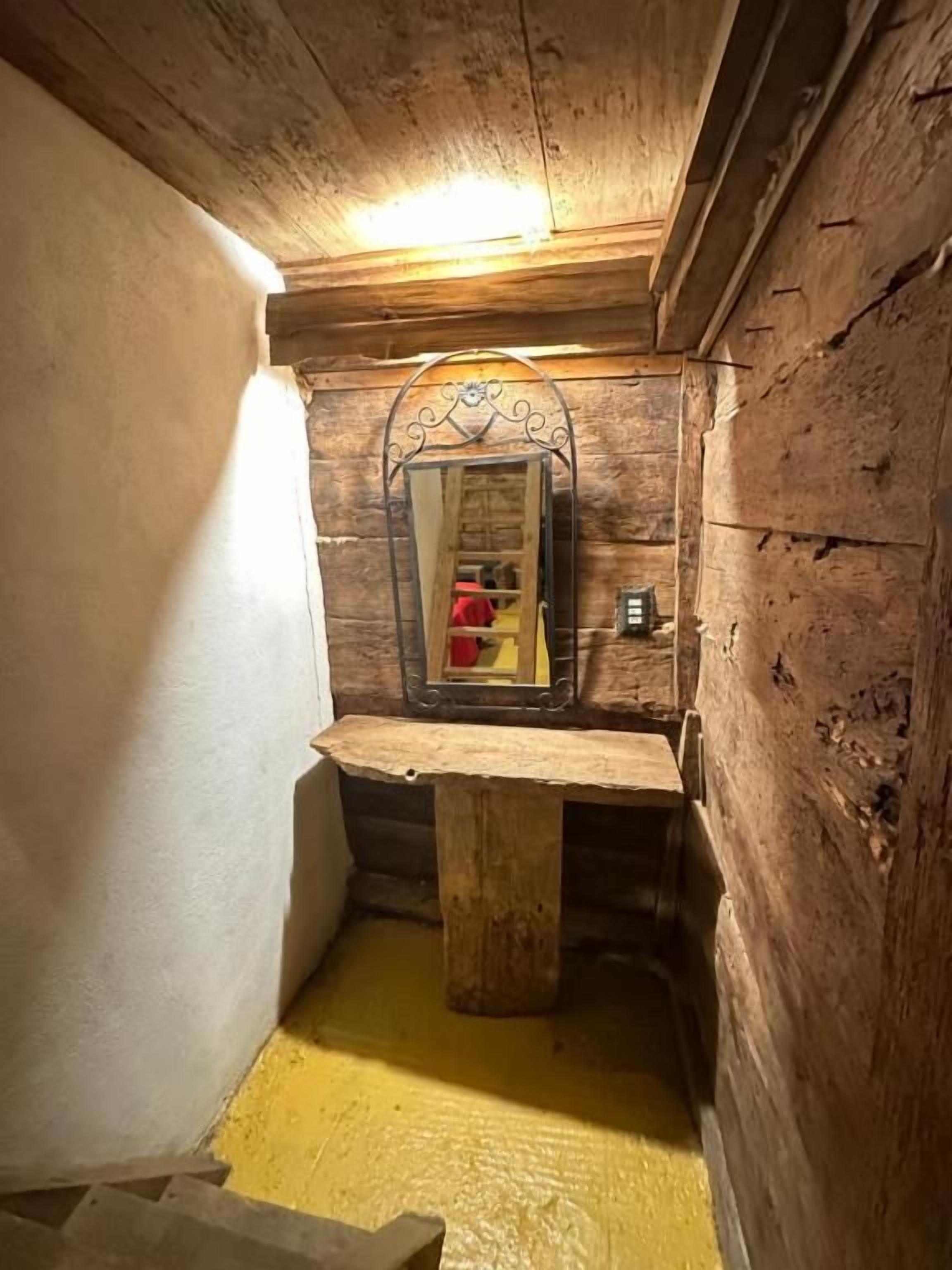 Una habitación pequeña de madera con un banco, un espejo y una mesita.