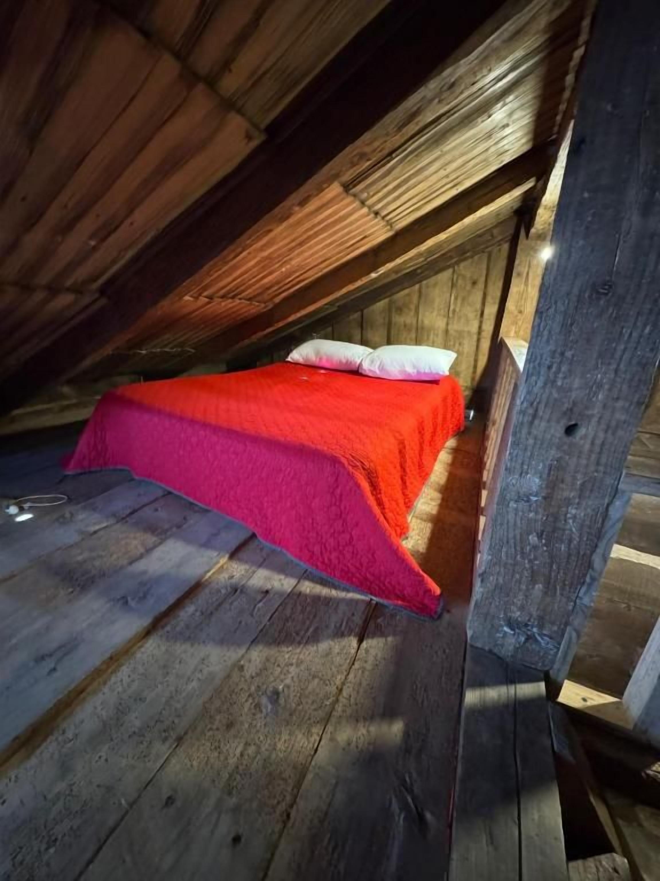 Une petite pièce mansardée fermée, avec un lit simple et un plafond en bois incliné.