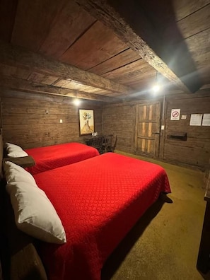 A room with two beds, wooden walls, a door, and a light fixture. - Cabañas del Valle  (San Pedro Atmatla)