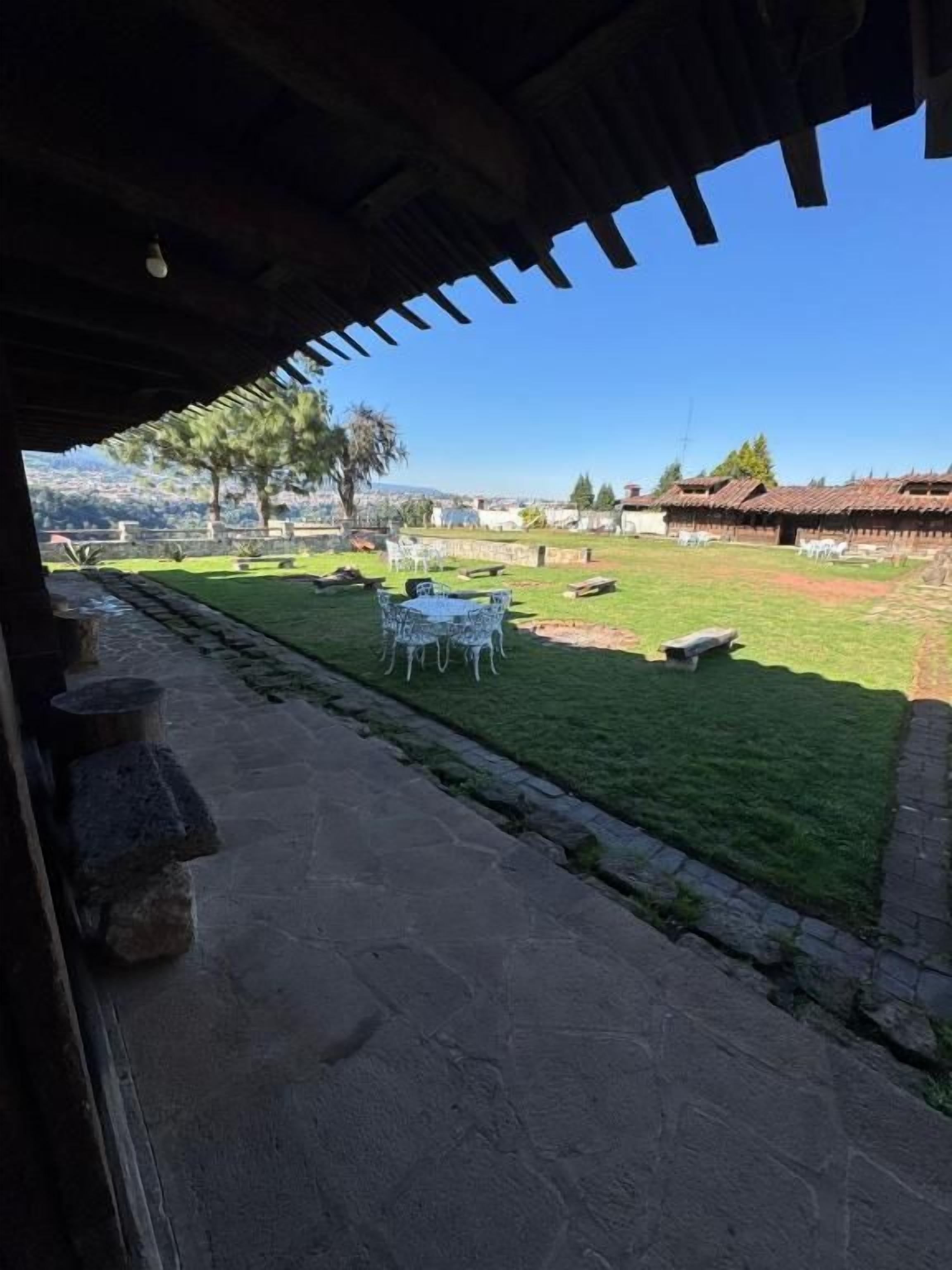 An outdoor patio area with stone flooring, a grassy lawn, and a view of a distant building.