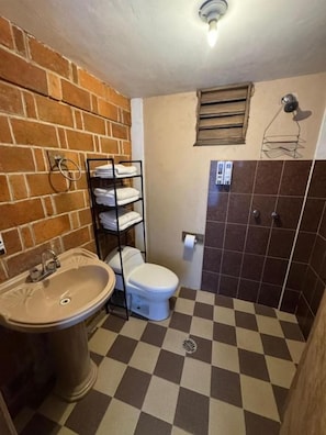 A bathroom with a sink, toilet, and a towel rack against a brick wall.