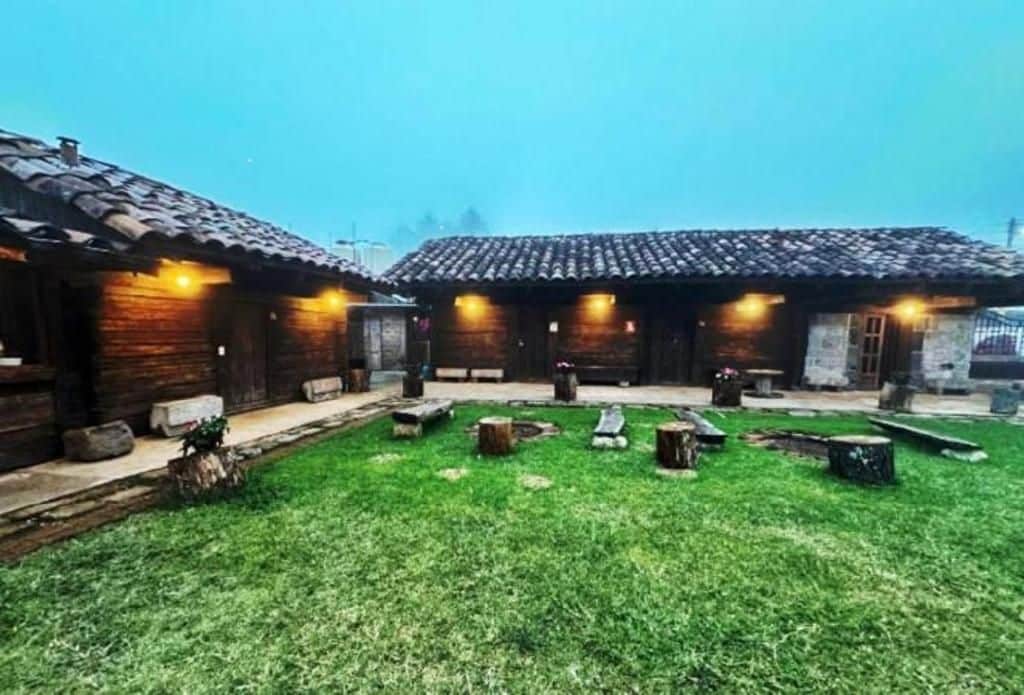 A courtyard with wooden buildings, a grassy area, and stone benches.