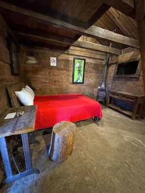 A rustic wooden room with a bed, a bench, a small table, and a fireplace.