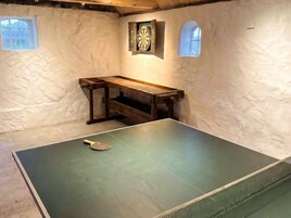 Una mesa de ping pong en una habitación con paredes blancas y dos ventanas pequeñas.