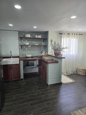 A modern kitchen with grey tiles, wooden cabinets, a built-in oven, and a window with sheer curtains. - HISTORIAL COLONIAL ZONE UNIT, LARGE TERRACE, VIEW OF THE CARIBBEAN SEA (Santo Domingo)