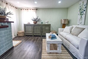 A living room with a white sofa, a coffee table with books, a cabinet with decorative items, and a painting on the wall. - HISTORIAL COLONIAL ZONE UNIT, LARGE TERRACE, VIEW OF THE CARIBBEAN SEA (Santo Domingo)