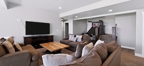 Ein modernes Wohnzimmer mit Flachbildfernseher, Couchtisch aus Holz und grauem Sofa mit gemusterten Kissen.