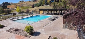 Ein rechteckiger Swimmingpool mit umlaufender Liegefläche, Liegestühlen und einem überdachten Sitzbereich.