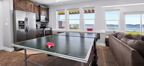 A ping pong table in a room with a kitchen, a couch, and a view of the outdoors. - Two Bear Lodge | Sleeps 35 | Beach, Pools & Views (Fish Haven)