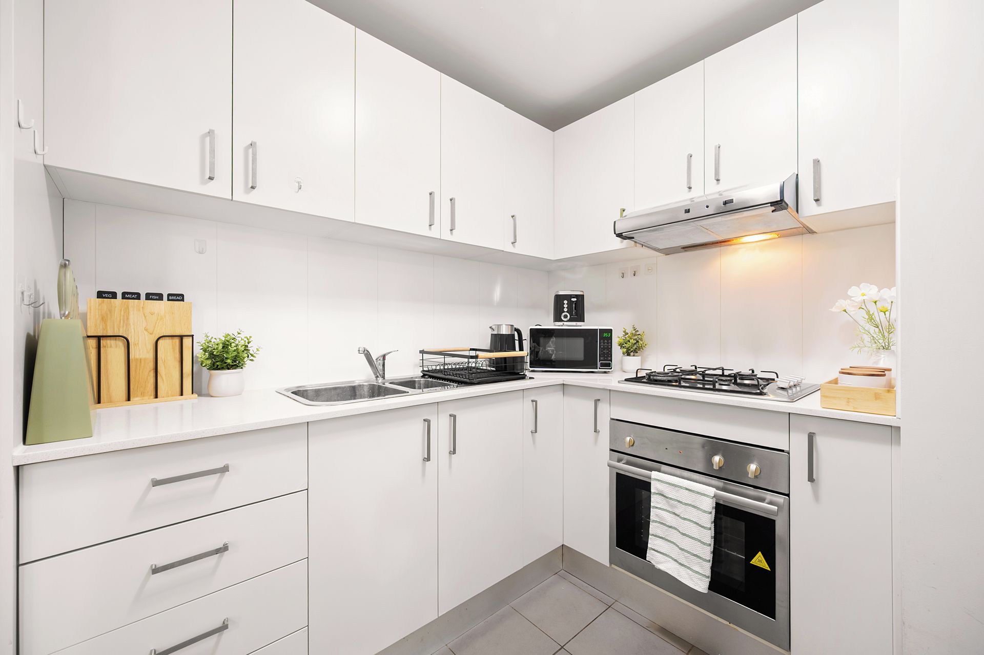 Een moderne keuken met witte kastjes, roestvrijstalen apparatuur en een gasfornuis.