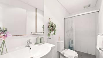 A modern bathroom with a white sink, a mirror, a shower, and a toilet.