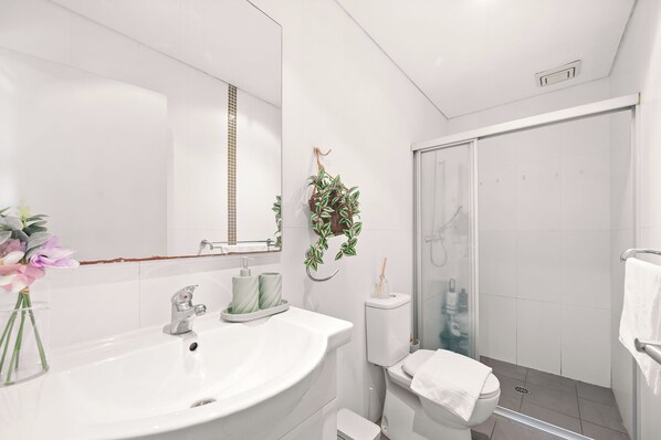 A modern bathroom with a white sink, a mirror, a shower, and a toilet.