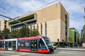 A tram in motion with a modern building in the background. - Private Terrace 2BR + Free Parking | Walk to UNSW (Kingsford)