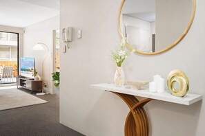 A modern hotel lobby with a reception desk, a large mirror, a vase with flowers, and a television displaying a scenic view.