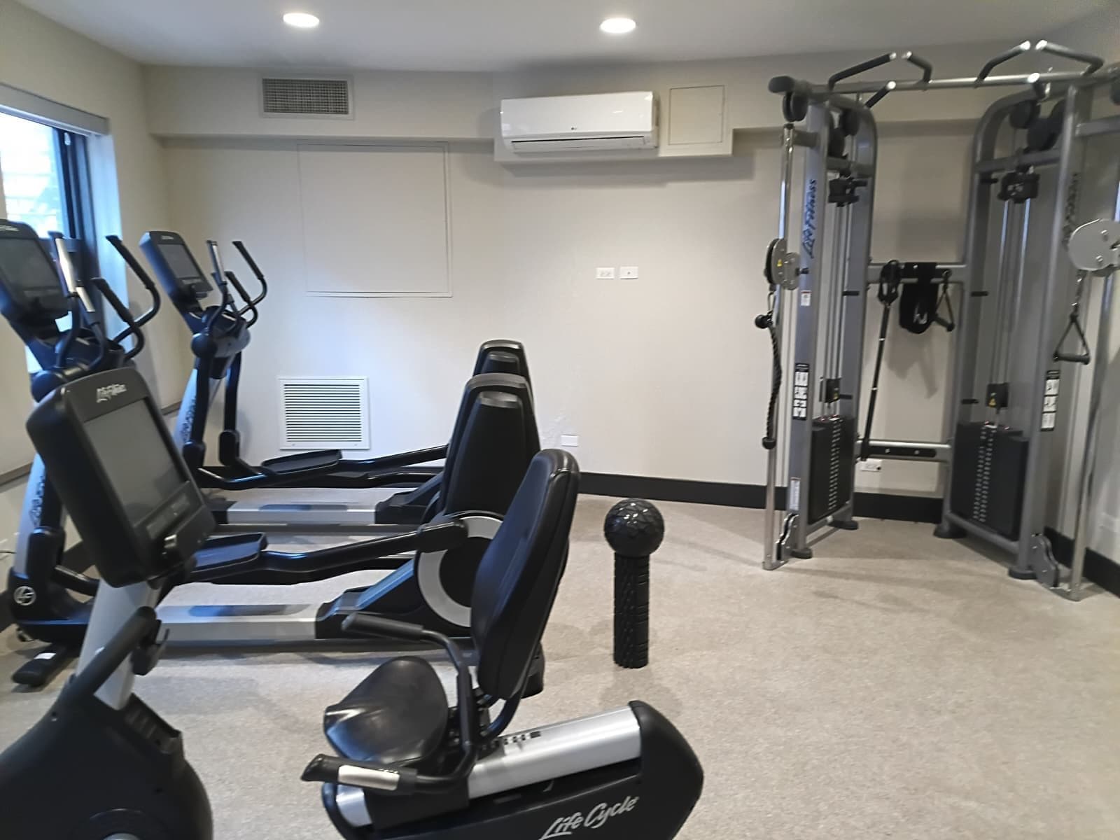 Een sportschool met hometrainers, een krachttrainingapparaat en een wandairconditioner.