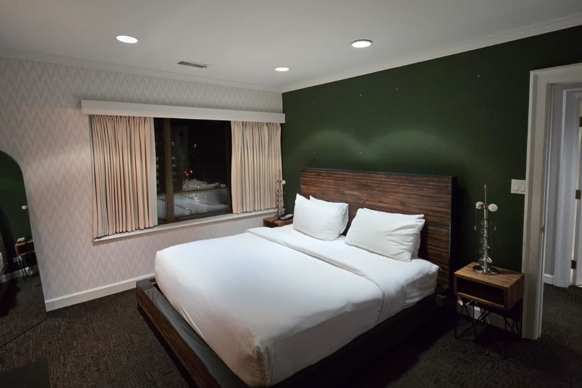 Ein modernes Hotelzimmer mit einem großen Bett, einem Nachttisch, Vorhängen und einem Fenster.