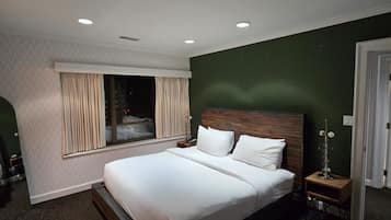 A modern hotel room with a large bed, a bedside table, a nightstand, and a window with curtains.