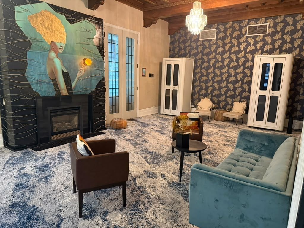 Uma sala de estar com lareira, sofá, poltrona e um painel decorativo na parede.