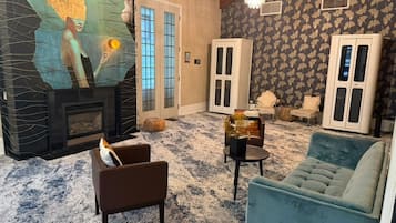 Uma sala de estar com lareira, sofá, poltrona e um painel decorativo na parede.
