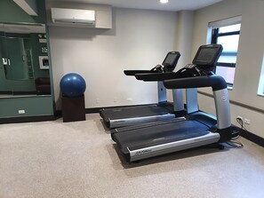 Un gimnasio con cintas de correr, una pelota de ejercicios azul y un equipo de aire acondicionado instalado en la pared.