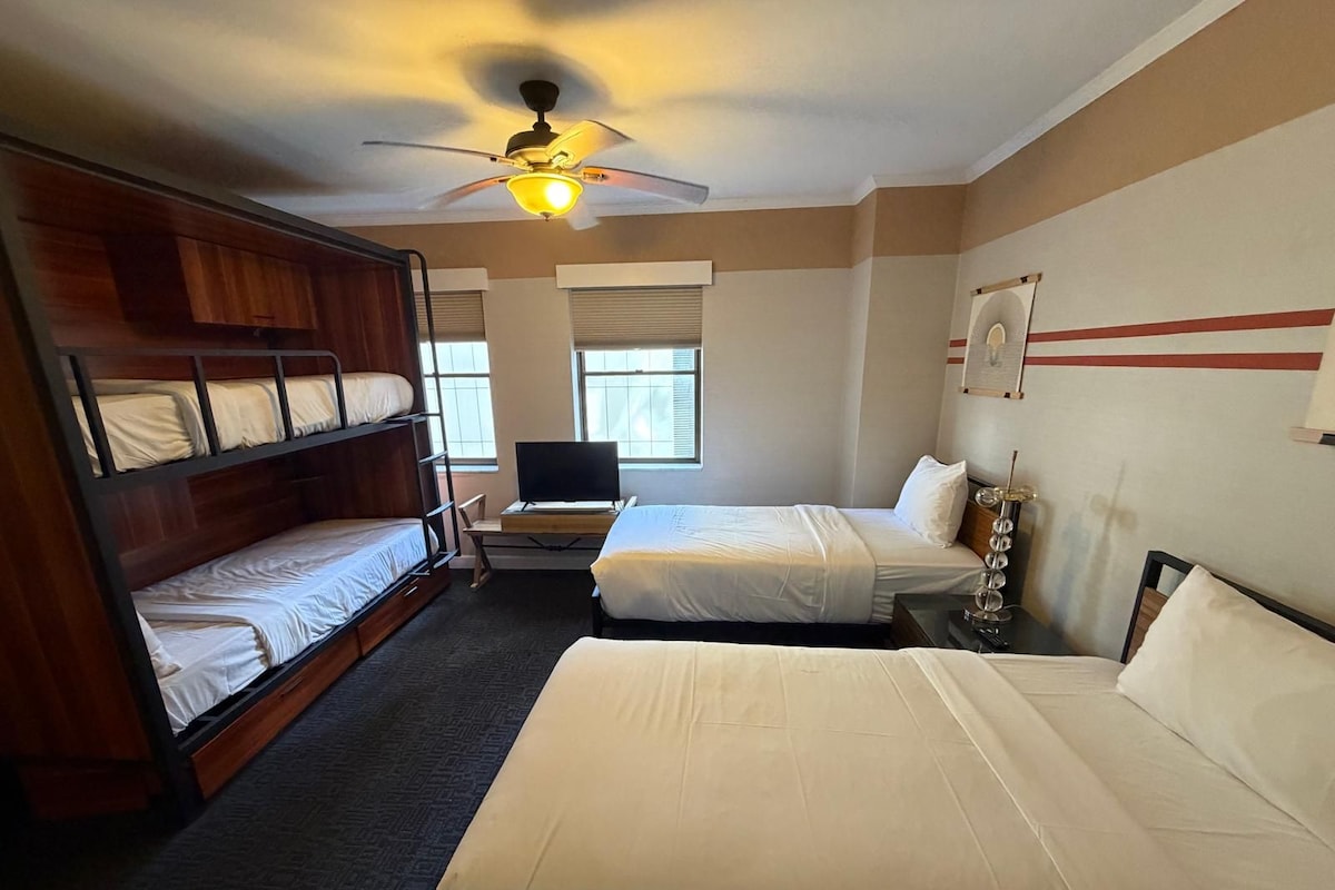 Ein Hotelzimmer mit Etagenbetten, einem Schreibtisch mit Computer und einem Deckenventilator.