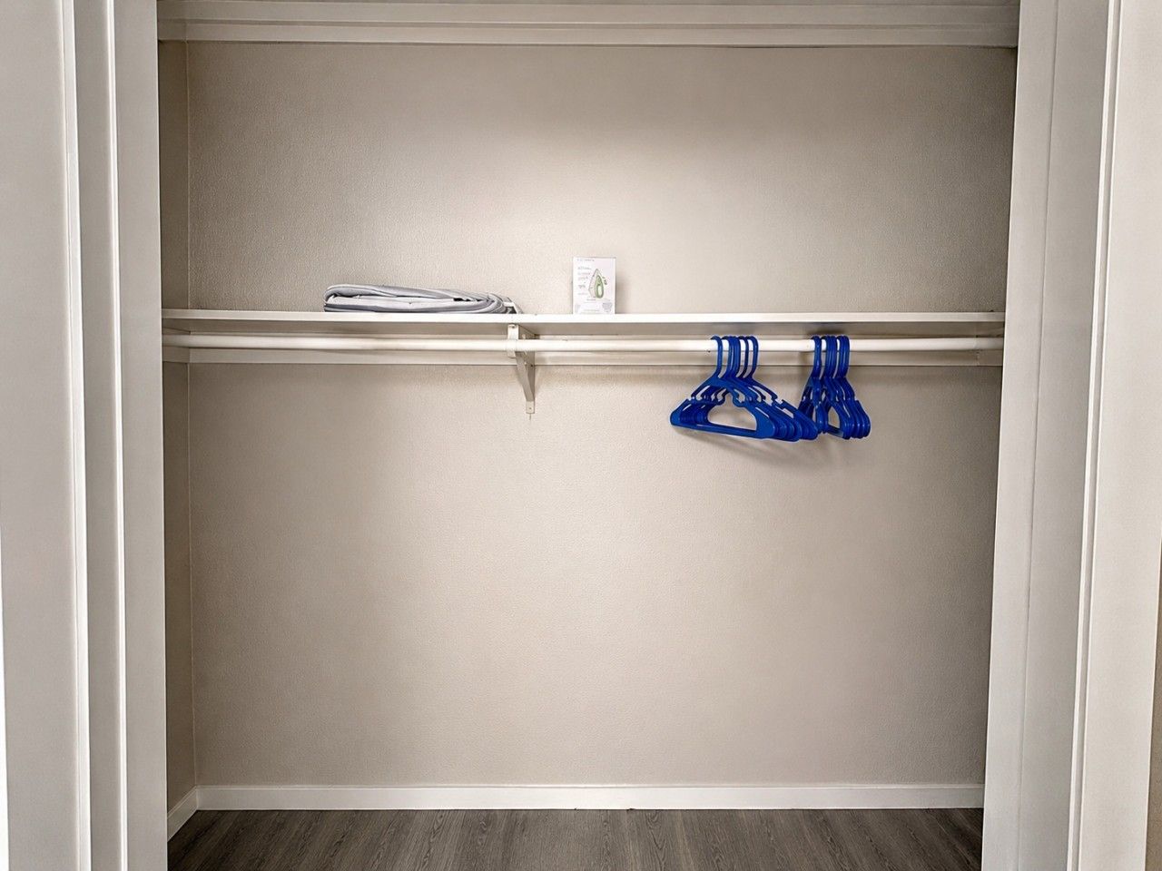 A closet with a white door, a shelf with folded clothes, and a blue hanger on a rod.