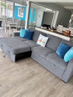 Ein graues Ecksofa mit blauen Kissen, ein Holzesstisch und Stühle.