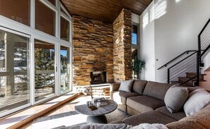A modern living room with a stone fireplace, a large window, and a staircase. - IL CERVO - The Stag (Park City)
