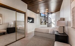 A bedroom with a large mirror, a bed, a nightstand, and a staircase leading to an upper level. - IL CERVO - The Stag (Park City)