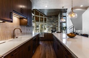 Une cuisine moderne dotée d’un long comptoir, de meubles en bois et d’un mur d’accent en pierre.