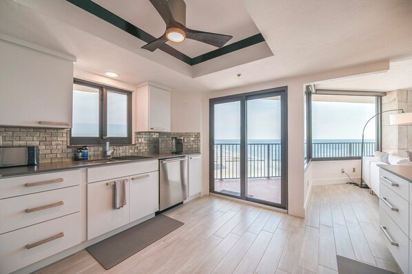 Une cuisine moderne dotée d’un grand îlot central, d’un ventilateur de plafond et offrant une vue sur la mer grâce à ses portes-fenêtres coulissantes.