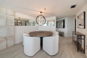 Un espace de salle à manger moderne avec une table ronde et des chaises à revêtement blanc, un lustre et un grand miroir.