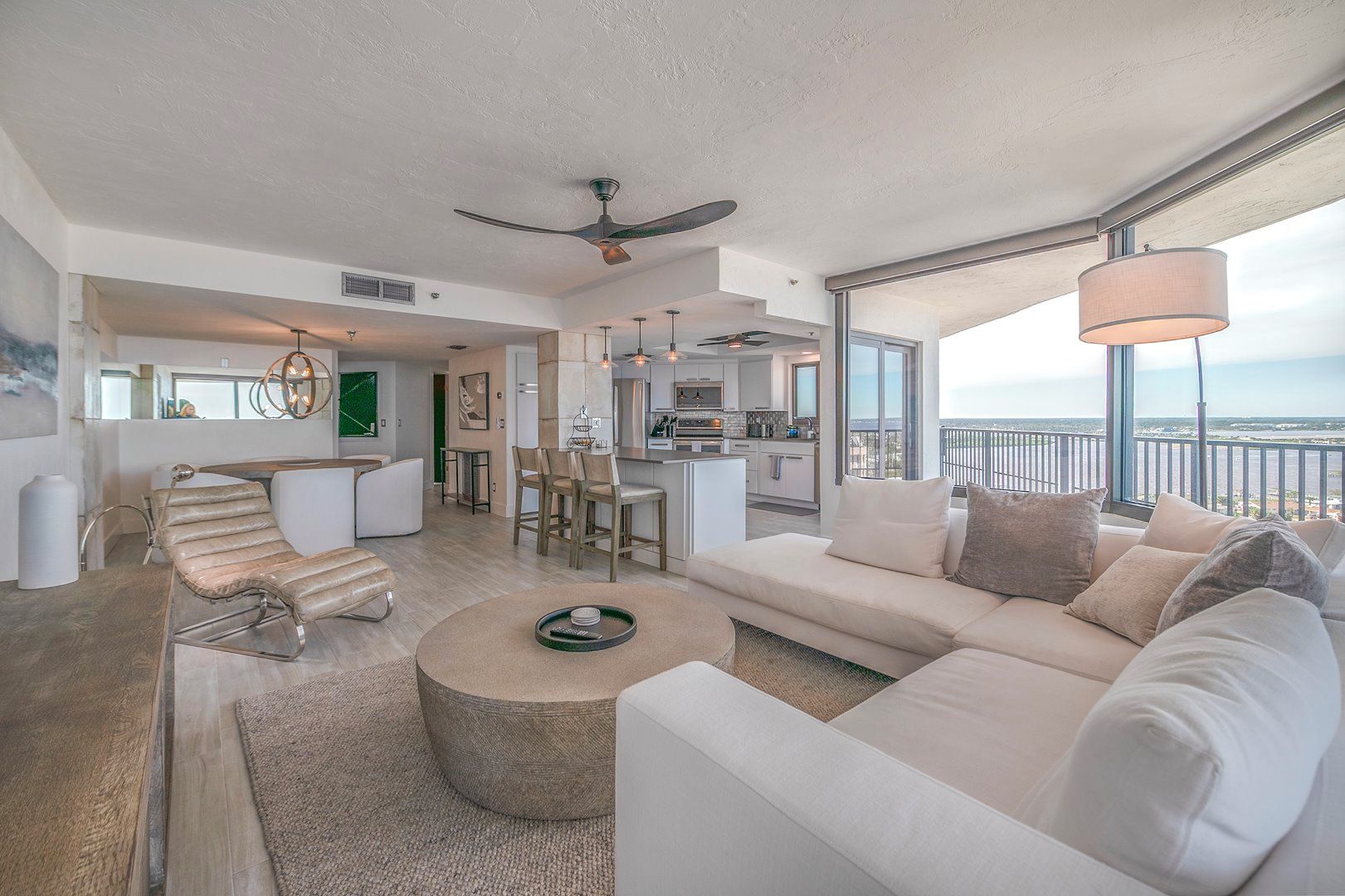 A modern living room with a large sofa, a round coffee table, and a dining area with bar stools.
