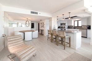 A modern kitchen with white cabinetry, a central island, and bar stools. - 17th Floor Oceanview Condo 2/2 -2 King Beds (Daytona Beach Shores)