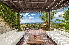 A covered outdoor seating area with a view of the ocean, a table with a flower, and a bench. - L'Horizon Luxury Sea View Villa (Bridgetown)