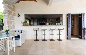 A bar area with a counter and stools, a seating area with a table and chairs, and a view into the kitchen. - L'Horizon Luxury Sea View Villa (Bridgetown)