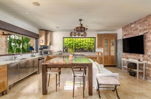 A modern kitchen with a large island, wooden cabinets, a built-in oven, and a large window with a view of greenery. - L'Horizon Luxury Sea View Villa (Bridgetown)