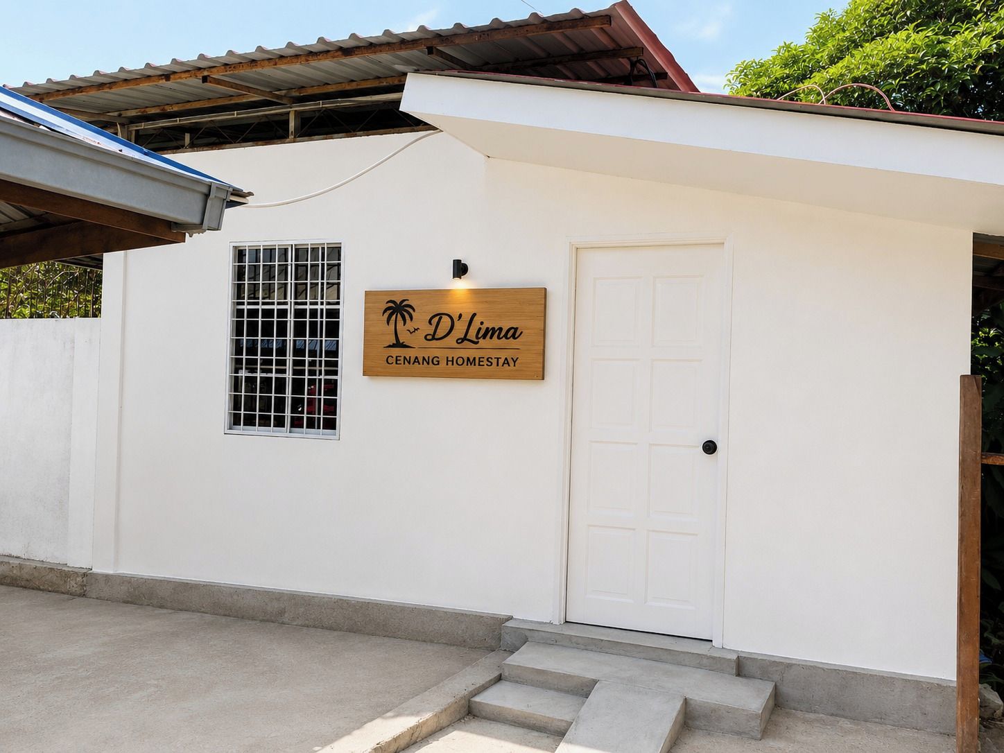Ein weißes Gebäude mit einem hölzernen Schild, auf dem 'D'Limac Cenang Homestay' steht, und einer weißen Tür.