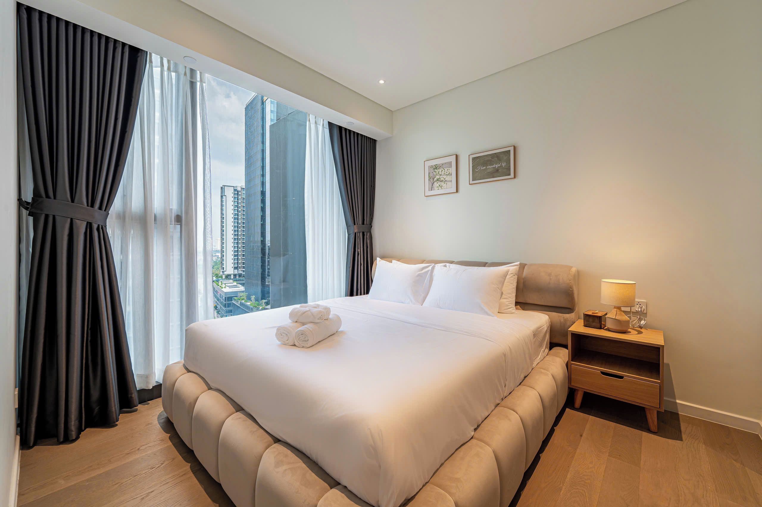 A hotel room with a large bed, a nightstand, and a view of the cityscape.